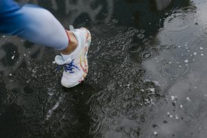 Close-up of a runner's shoe splashing through a puddle on a rainy day.